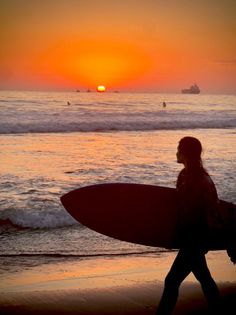 Surfer walking on the beach at sunset with a surfboard