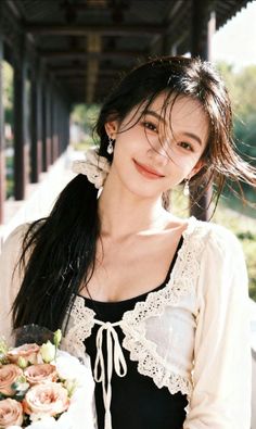 Woman with long hair in a lace top holding a bouquet outdoors