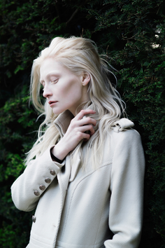 Woman with long blonde hair and pale skin wearing a white coat outdoors