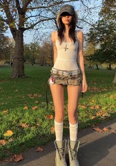 Woman in a mini skirt, tank top, and boots standing in a park