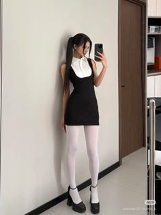 Woman in a black dress and white tights taking a mirror selfie