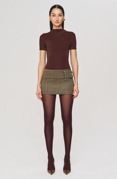 Woman in a brown top, mini skirt, and tights posing against a white background