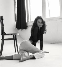Woman in a sheer top and jeans posing on the floor in a room with a window