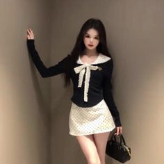 Woman with long dark hair wearing a black top and polka dot skirt indoors