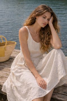 Woman in a white dress sitting on a wooden dock by the water