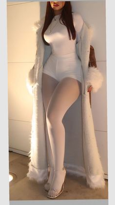 Woman in a white outfit and long coat with fur trim, posing indoors