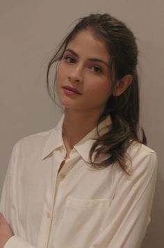 Woman with long brown hair wearing a white collared shirt, looking at the camera