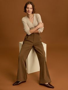 Woman with short hair wearing a cardigan and brown pants, sitting on a white block