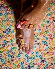 Feet with pink nail polish in a bowl of colorful cereal and milk