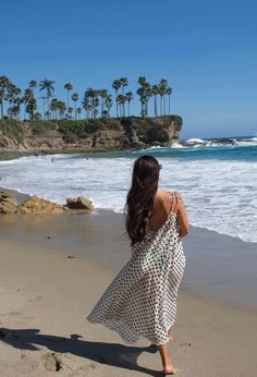 Woman in a polka dot dress walking on a sandy beach with palm trees and ocean waves