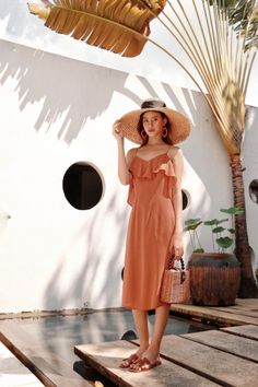 Woman in a ruffle dress and straw hat holding a wicker bag outdoors