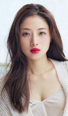 Woman with long brown hair and red lipstick wearing a white cardigan