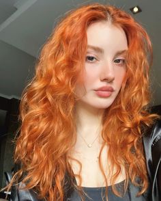 Woman with long curly red hair wearing a necklace, looking at the camera