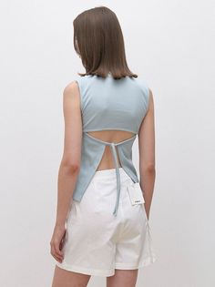Woman with short brown hair wearing a light blue open-back top and white shorts