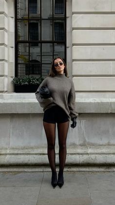 Woman in an oversized sweater, shorts, and tights standing outdoors