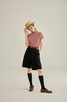 Woman in a straw hat, striped shirt, and black shorts posing in a studio