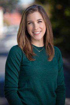 Woman with long hair wearing a green sweater and a necklace, smiling outdoors