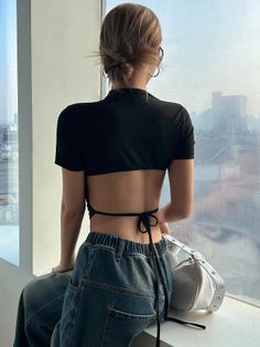 Woman in a black open-back crop top and jeans looking out a window