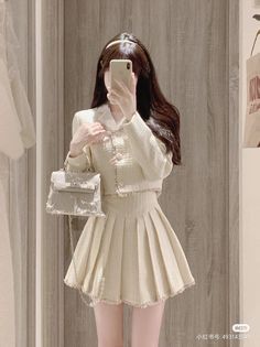 Person in a tweed jacket and pleated skirt taking a mirror selfie