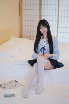 Woman in a school uniform and white thigh highs sitting on a bed