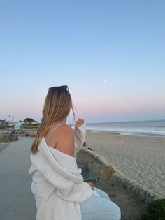 Woman with long hair looking at the moon over a beach at sunset