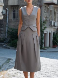 Woman in a gray sleeveless vest and pleated midi skirt on a cobblestone street