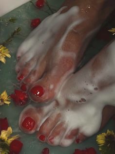 Feet with red nail polish in a bubble bath with flowers and petals
