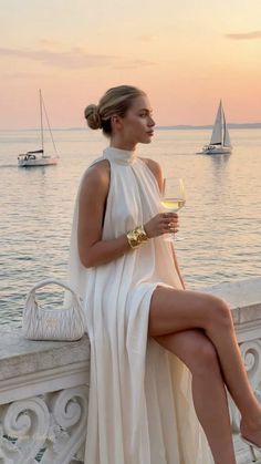 Woman in a white dress with a wine glass by the water at sunset