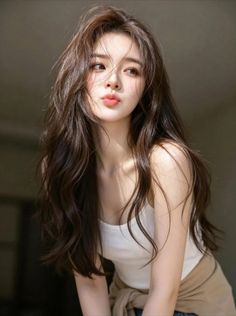 Woman with long brown hair and a white tank top making a pouty face