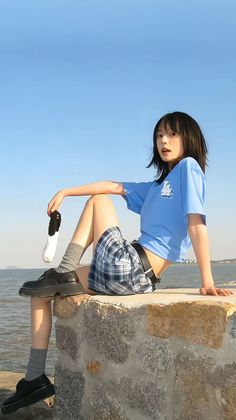 Woman in a plaid skirt and blue crop top sitting by the sea