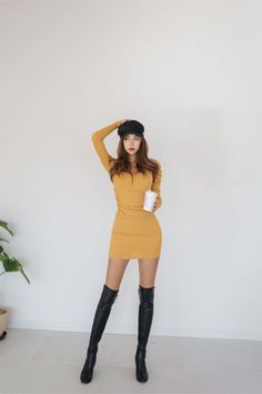 Woman in a yellow dress and thigh-high boots posing indoors with a white background