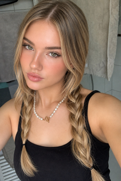 Woman with blonde braids and a pearl necklace wearing a black tank top