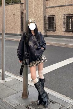 Person in a black hoodie and camo skirt leaning against a pole on a street