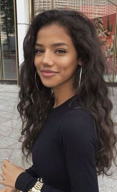 Woman with long curly hair and hoop earrings smiling outdoors