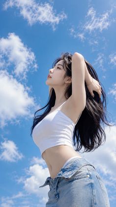 Woman in a white crop top and denim jeans against a blue sky with clouds