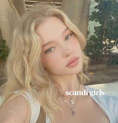 Blonde woman with wavy hair and blue eyes wearing necklaces outdoors