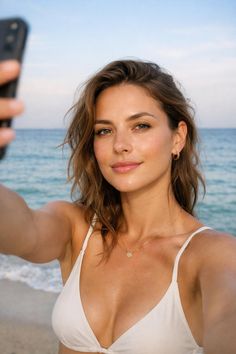 Woman in a white bikini taking a selfie at the beach