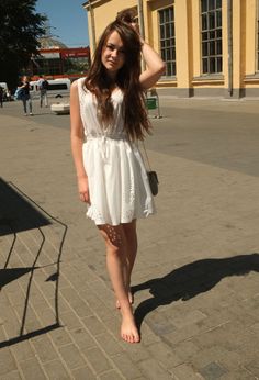 Young woman in a white dress standing barefoot on a street