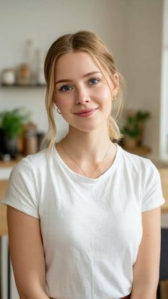 Blonde woman with blue eyes wearing a white t-shirt and gold jewelry indoors