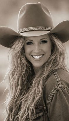 Woman in a cowboy hat and denim jacket with long wavy hair, smiling