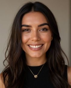 Woman with long dark hair wearing a black top and necklace, smiling at the camera