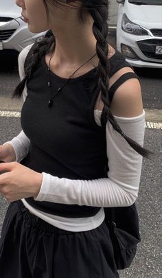 Woman with black braids wearing a black top over a white long sleeve shirt outdoors