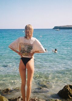 Woman in a t-shirt and bikini bottoms standing on a rocky beach