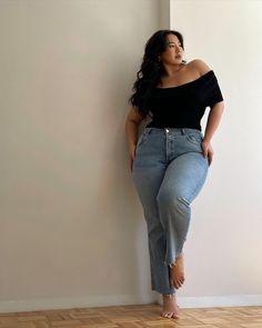 Woman with long dark hair wearing an off-shoulder top and jeans indoors
