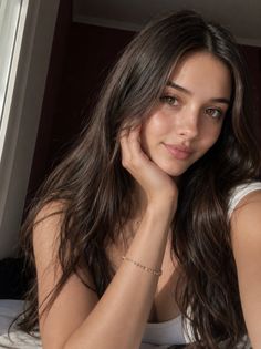 Woman with long brown hair and freckles wearing a white tank top indoors