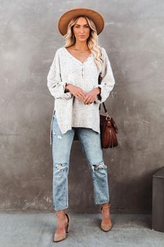 Woman with blonde hair wearing a brown hat, oversized sweater, and ripped jeans