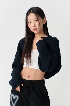 Woman in a white crop top and black cardigan with exposed midriff in a studio