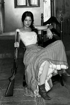 Woman with a shotgun sitting on a chair in a black and white photograph