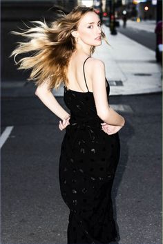 Woman in a black dress with long blonde hair blowing in the wind on a street
