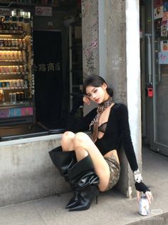 Woman in a black top and mini skirt with high heel boots sitting on a ledge